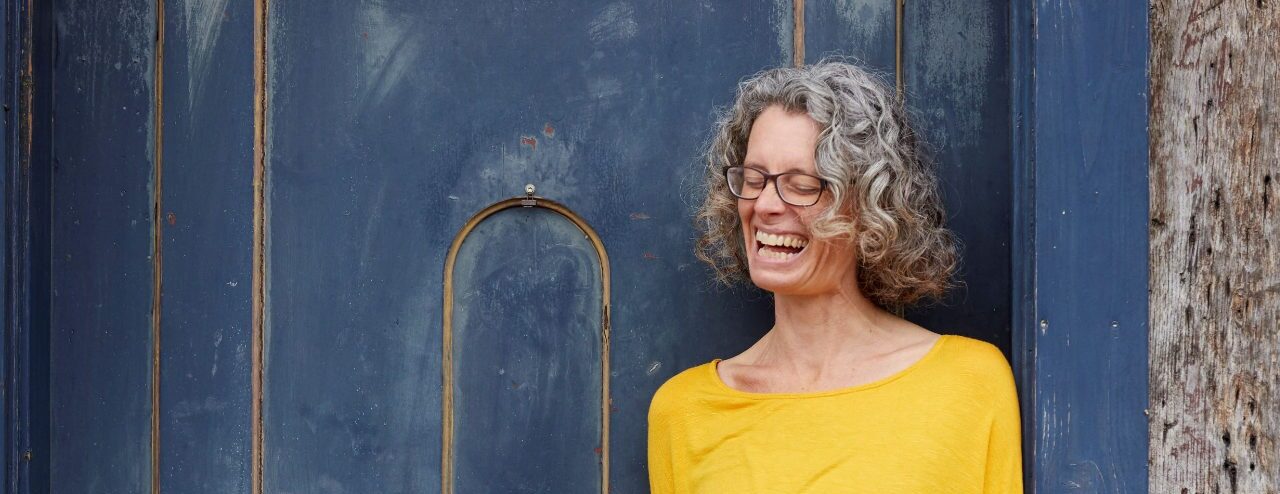 Evelyn lacht in gelb vor blauer tür Porträt Evelyn